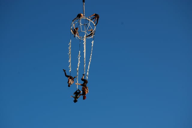Acrobàcia aèria amb persones penjant i fent figures en l'aire.